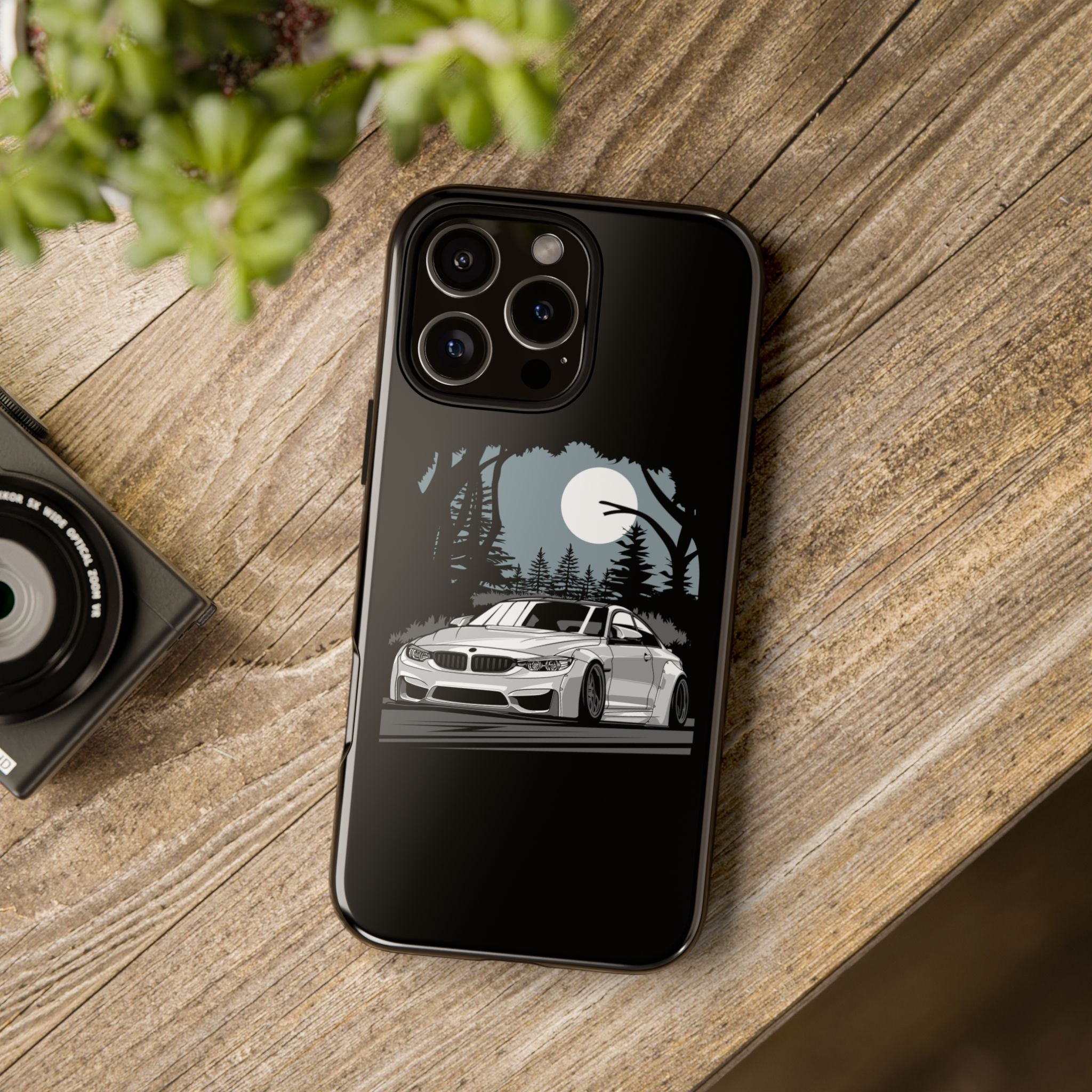 Phone case with car design on a wooden surface next to a camera