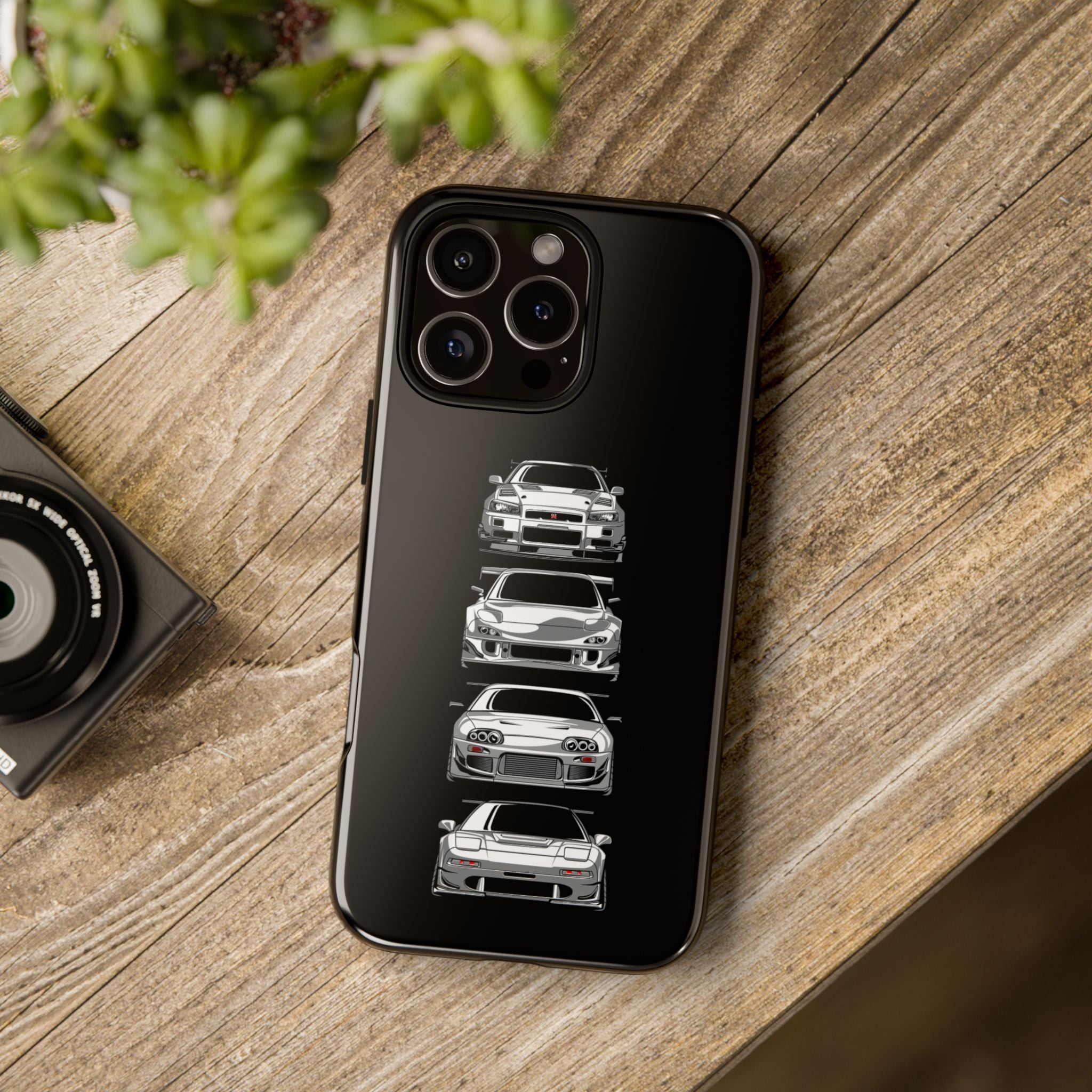 Phone case with car illustrations on a wooden surface next to a camera and plant