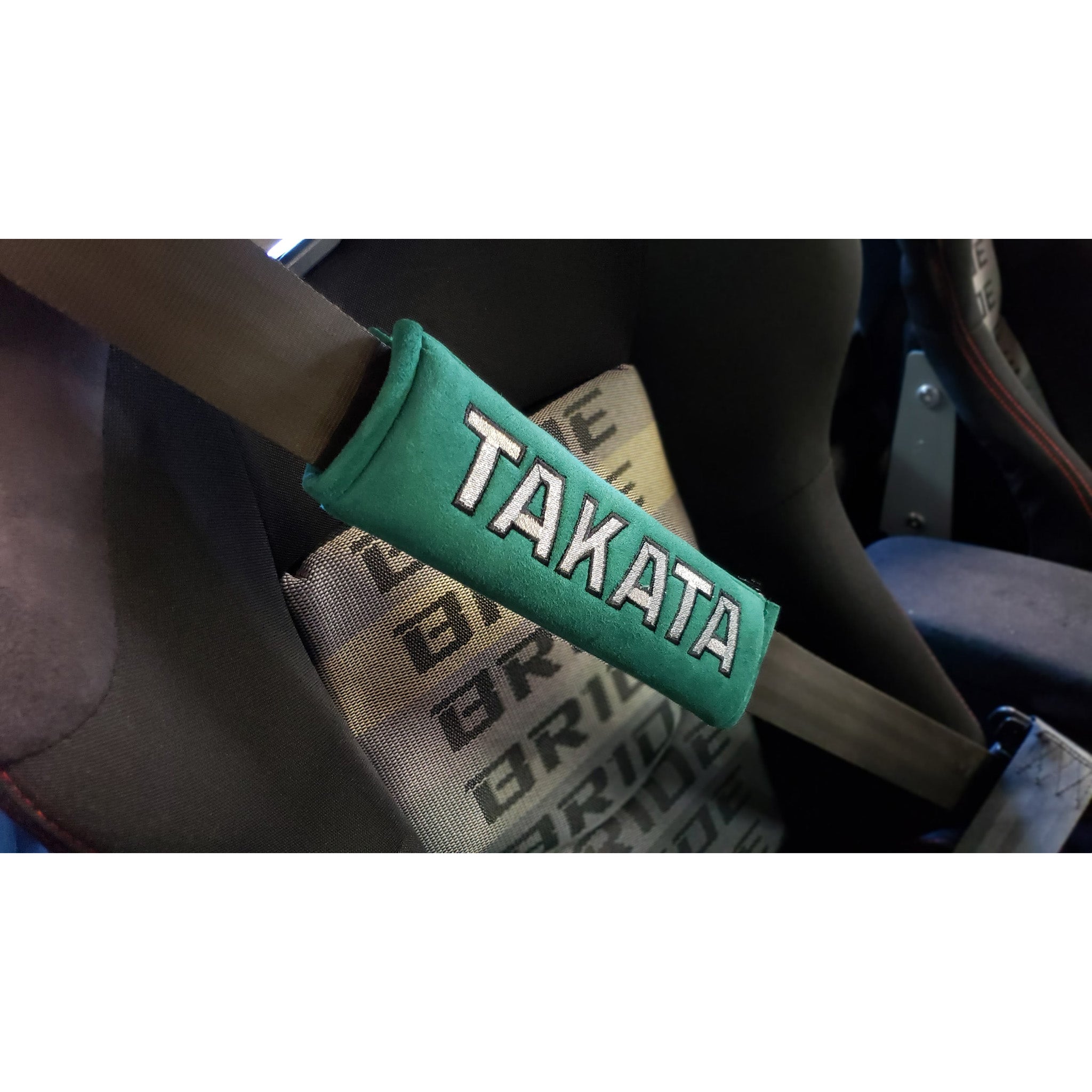 Takata comfort seat belt shoulder pads in green attached to seat belt in a car.